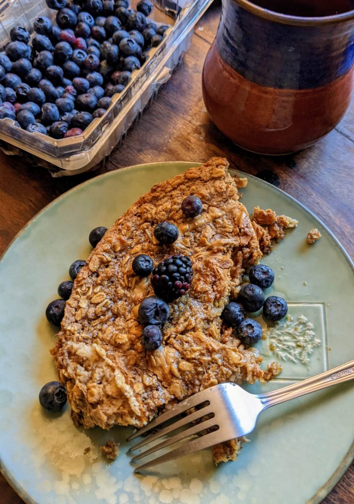 vegan baked oatmeal on a plate with blueberries, a blackberry, and a fork